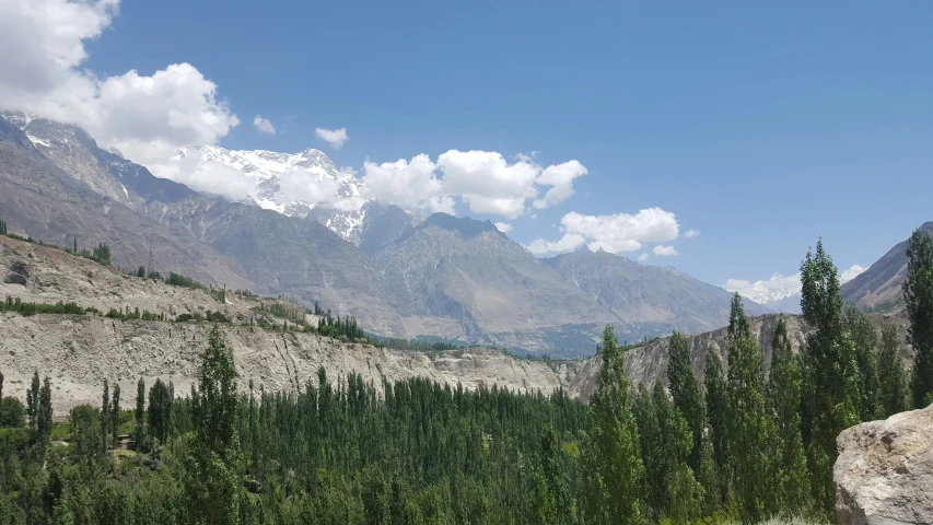 a landscape of mountains and trees with clouds in the background