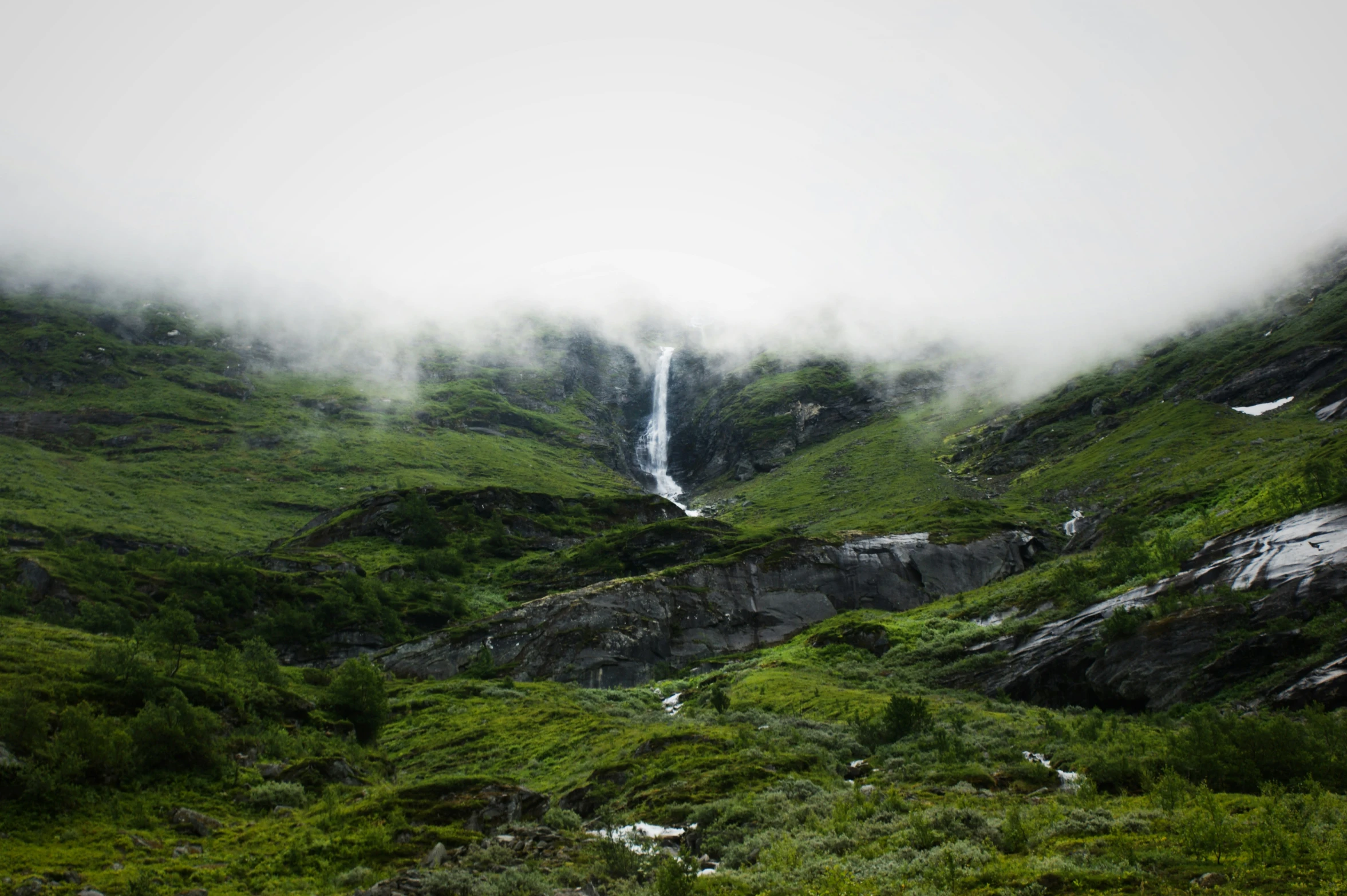 a view of a beautiful waterfall in the middle of mountains with fog