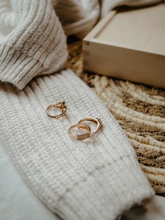 two gold earrings sitting next to a box