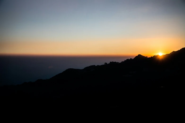 the sun is setting on a hill with some hills in the distance