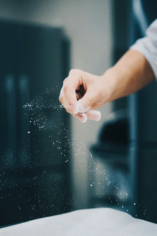 a hand sprinkling flour on a pizza dough