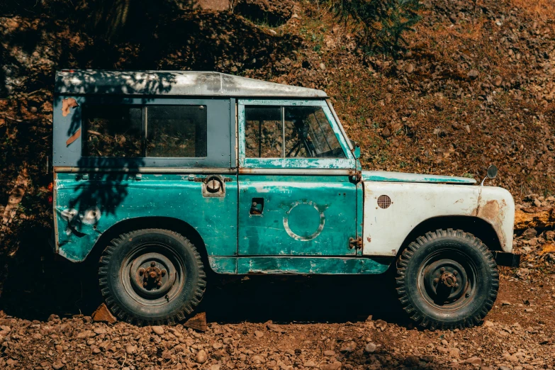 an old, rusty, and dusty green vehicle parked on top of a dirt field