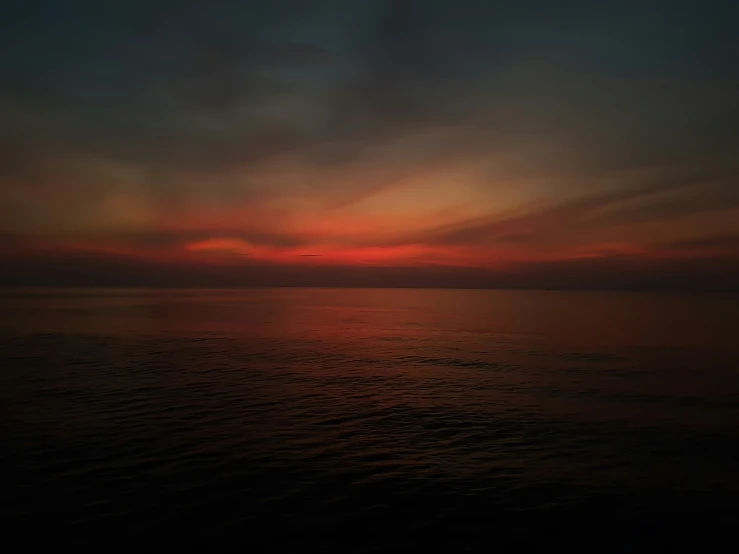 the sunset is seen over the ocean as dark clouds