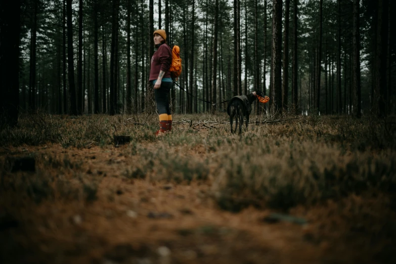 a young woman with an orange backpack and a dog in the woods