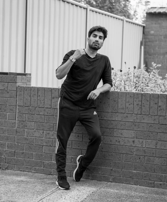 a man leaning against a brick wall with his legs crossed