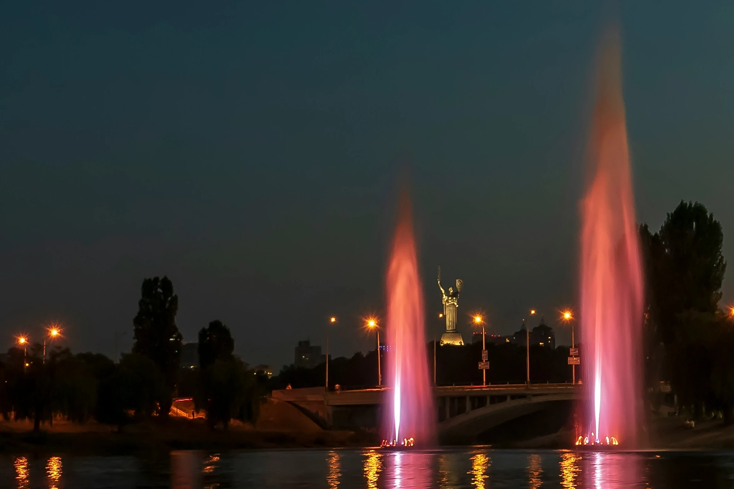 three fountains that are in the water near trees