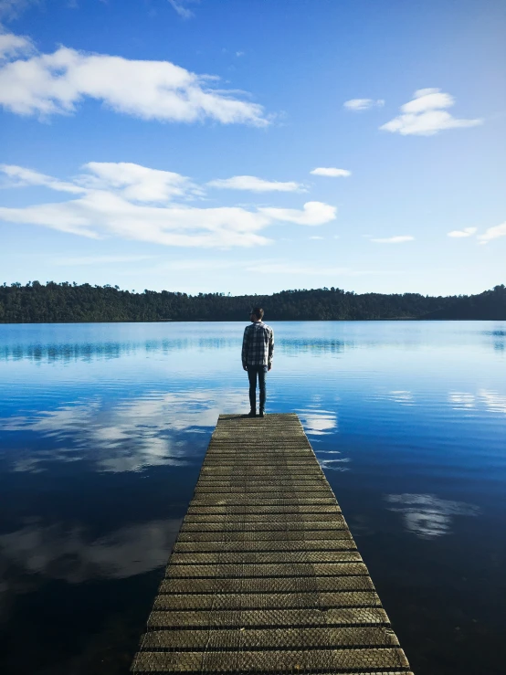 a lone person walking along a pier towards a calm lake