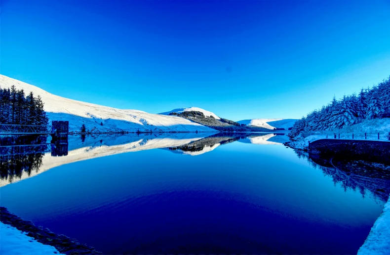 a snowy mountain range in the distance with trees around a small lake