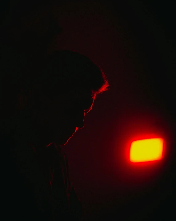 a man in dark looking down at a red light