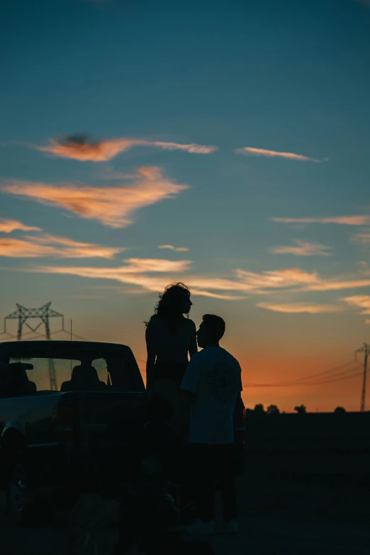 a couple is standing by a truck as the sun sets