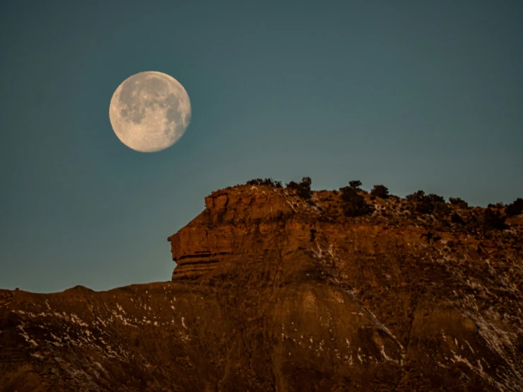 the moon is setting on the top of a mountain