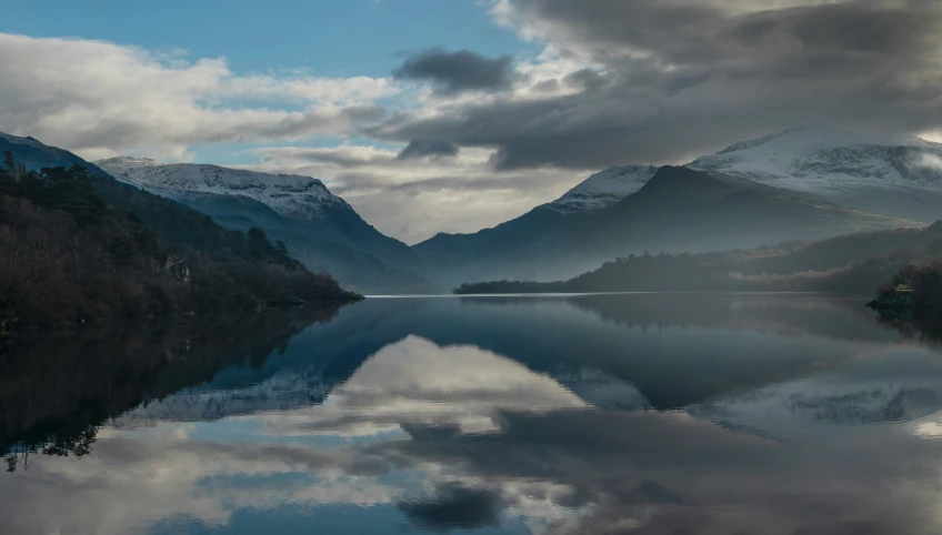 mountains and clouds are reflected in the still water