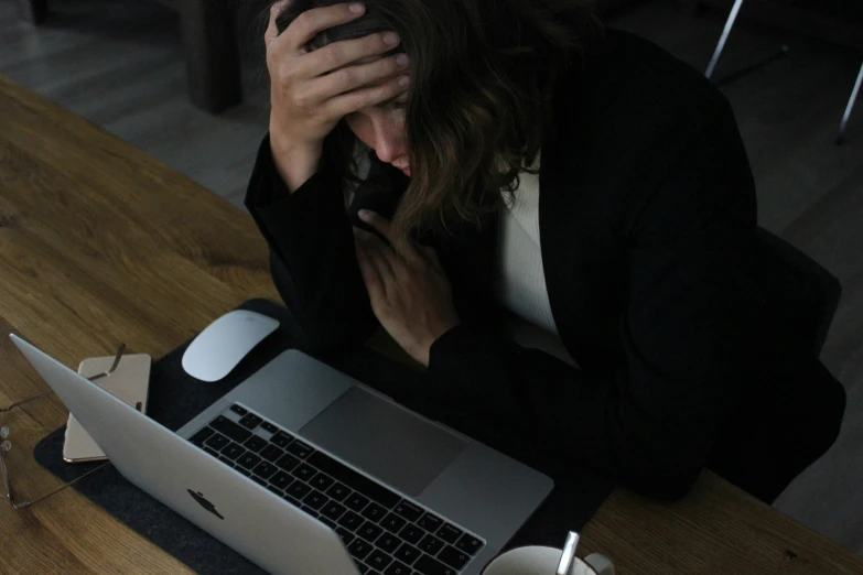 a person sitting with their hands on the face and in front of a laptop