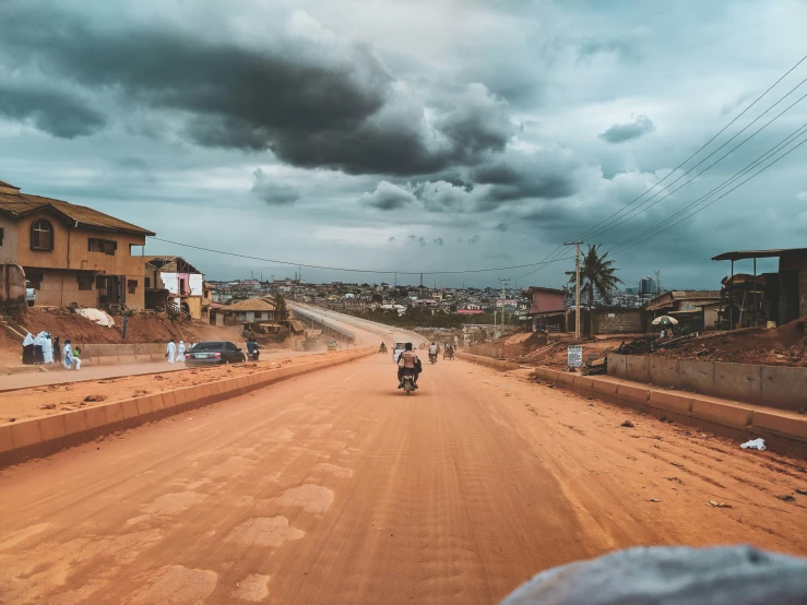 two men riding motorcycles down the road under stormy skies