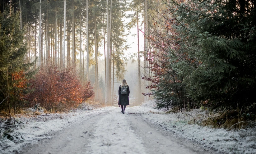 a person in black walking down a road covered with snow