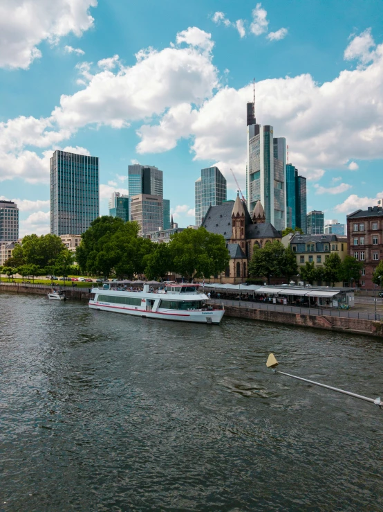 a river in the foreground with a ferry and a city skyline on one side