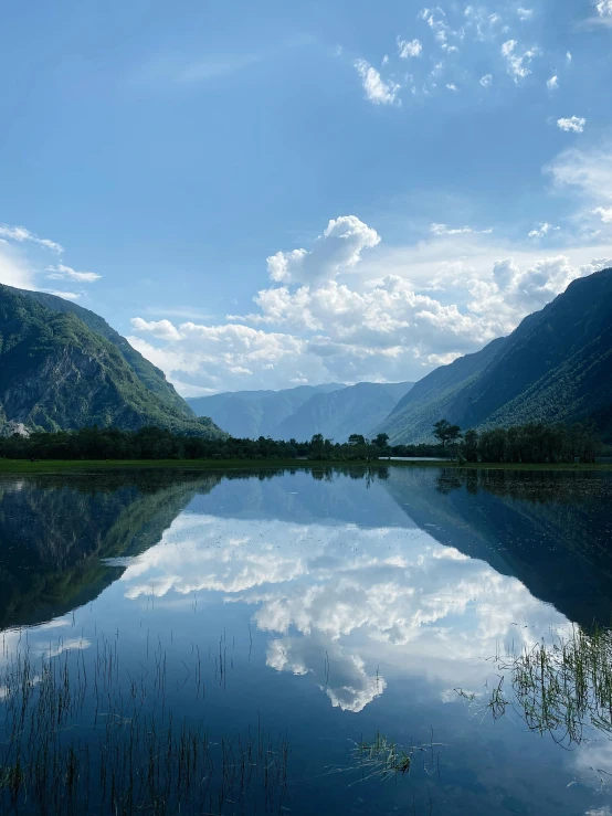 a large lake surrounded by green mountains under a cloudy blue sky