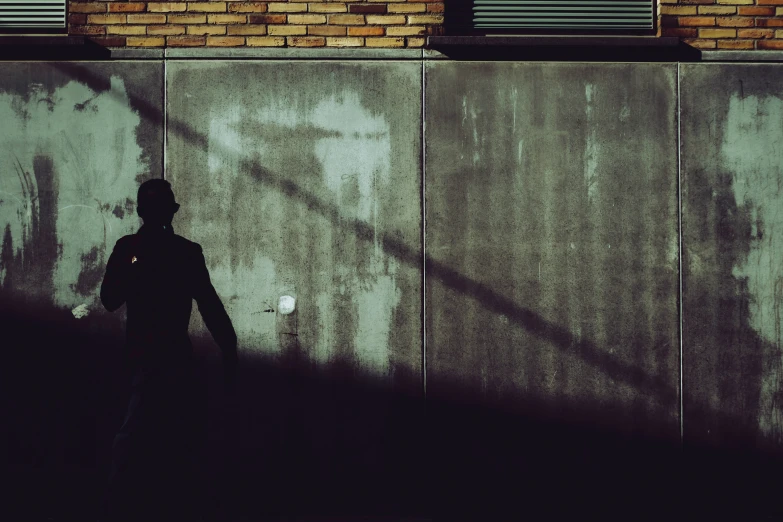 silhouette of person near brick building next to wall