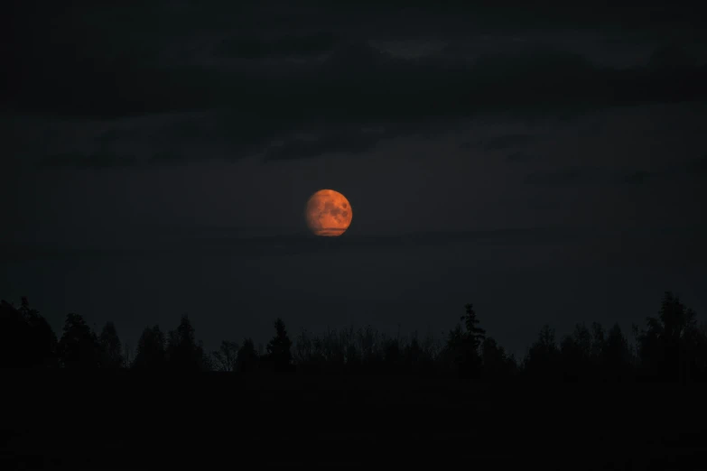 the full moon is setting in a cloudy sky