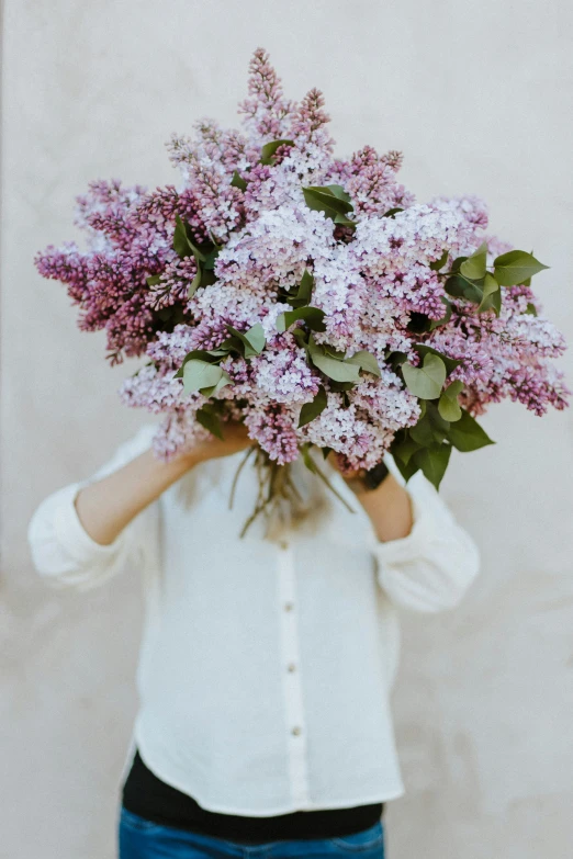 woman holding up large pile of lilacs with arms