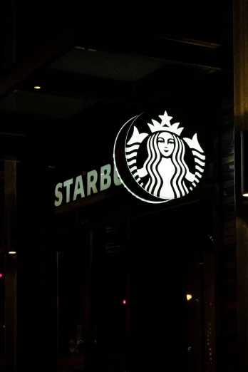 a starbucks sign lit up at night with the words starbucks on it