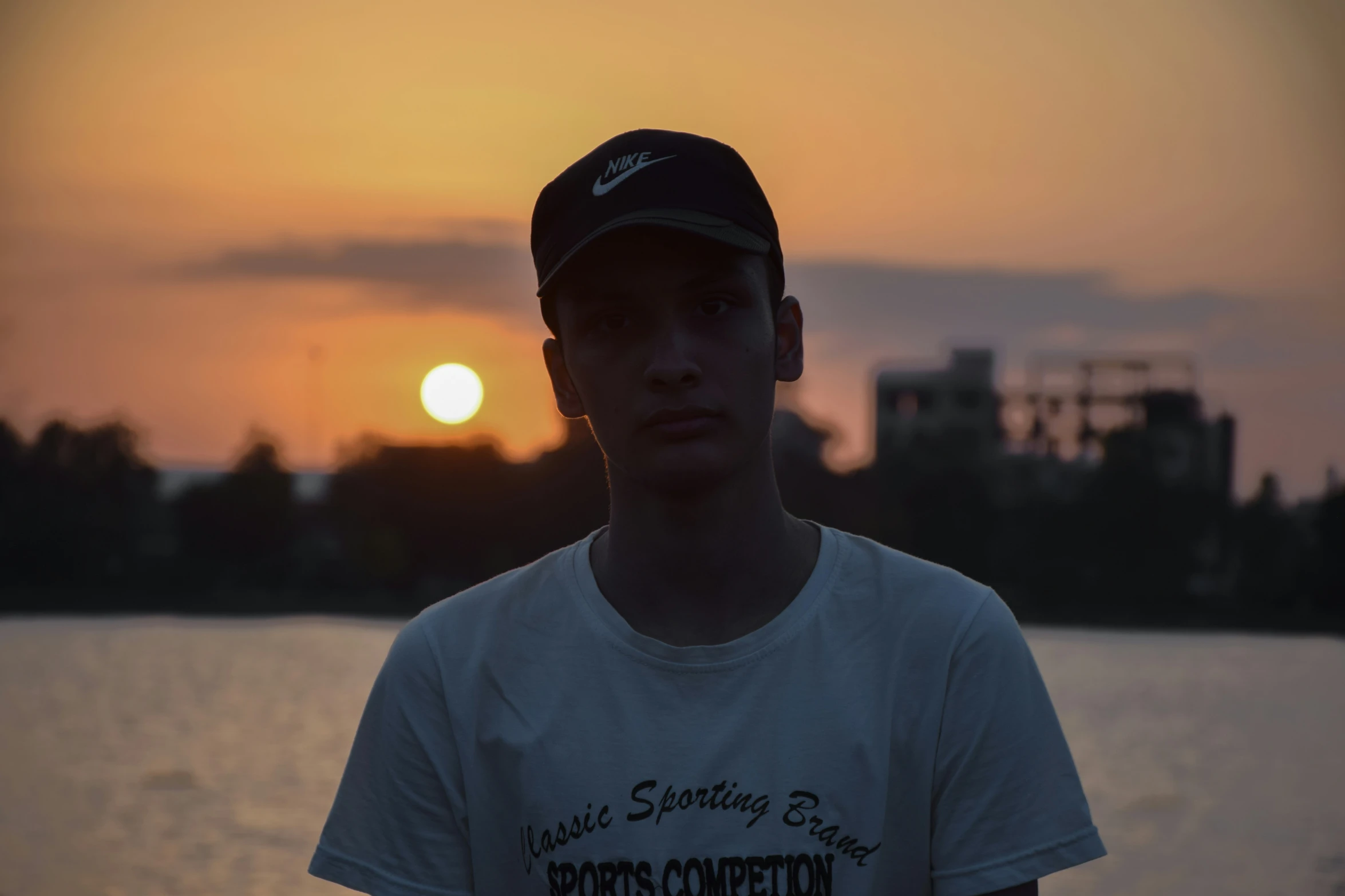 a boy is standing near the water with a sunset in the background