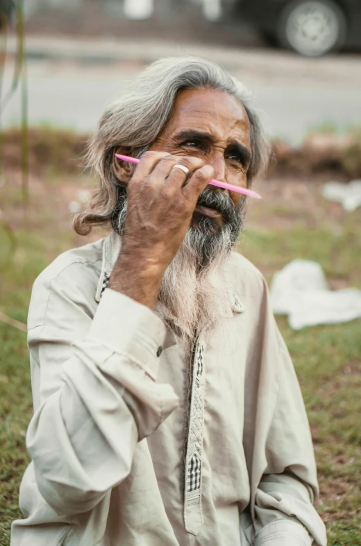 a man with gray hair holds up a pink pencil to his nose