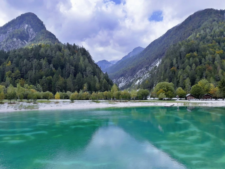 a green lake surrounded by mountains with clouds in the sky