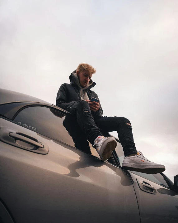 a man in a black jacket sitting on the roof of a car