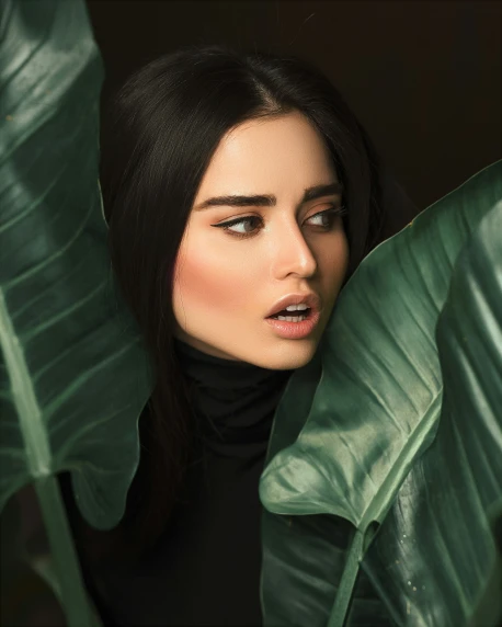 a beautiful young woman is standing behind a green plant