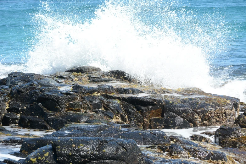 a big wave crashing onto some rocks on the shore