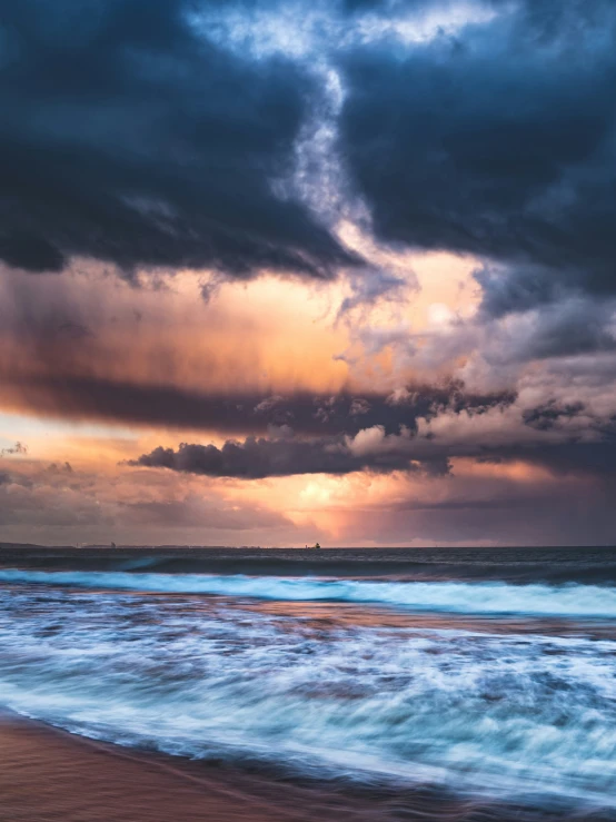 the sun is setting on the dark clouds over the ocean