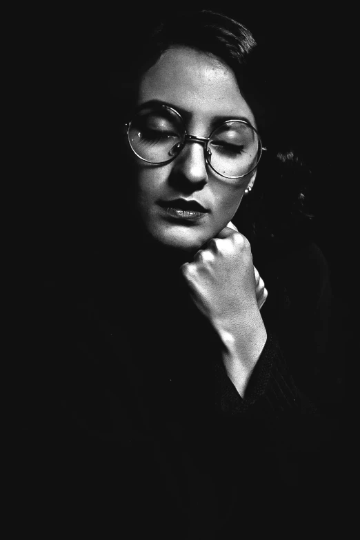 a woman in glasses leaning on a black wall