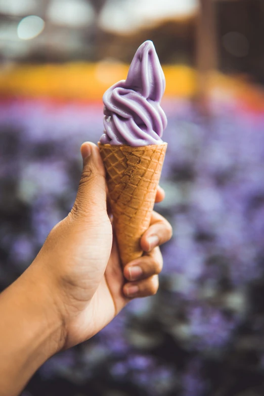 a hand holding up a purple ice cream cone