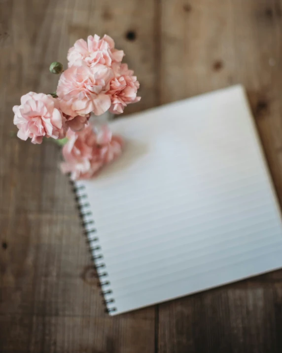 a notepad sitting on top of a wooden table with pink flowers