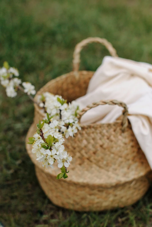 a straw basket with flowers and a blanket on grass