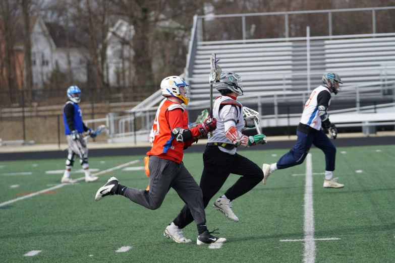 three lacrosse players run in a field with net and a ball