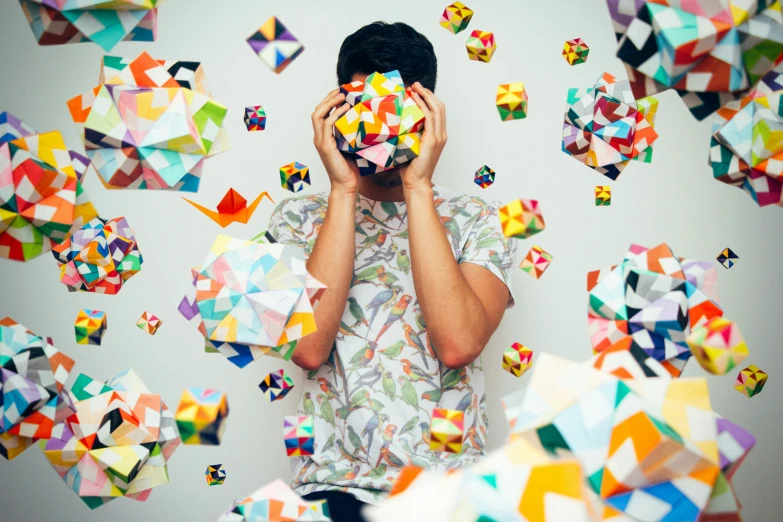 a man covers his face with colorful origami