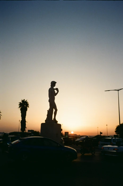 the sun is setting behind a statue in the middle of a parking lot