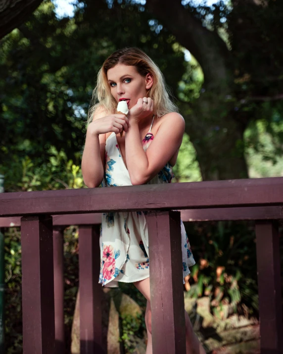 a woman leaning against a wooden railing holding soing up to her mouth