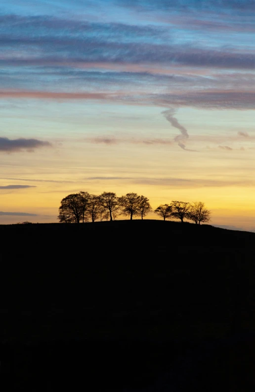 a sunset showing three trees on top of a hill