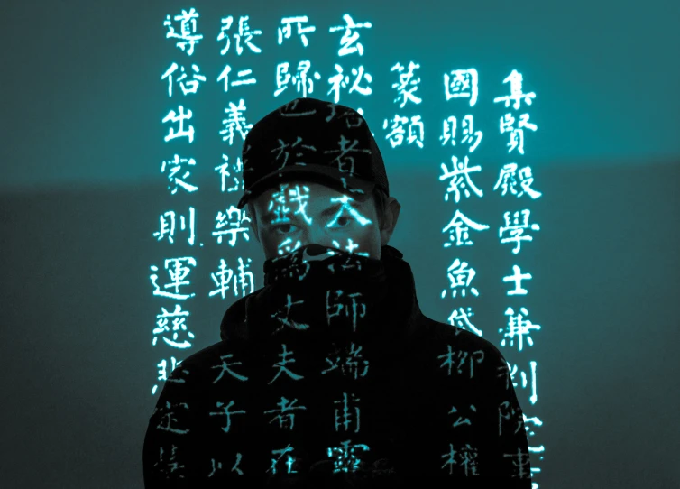 an asian man wearing a beanie standing next to an array of asian writing