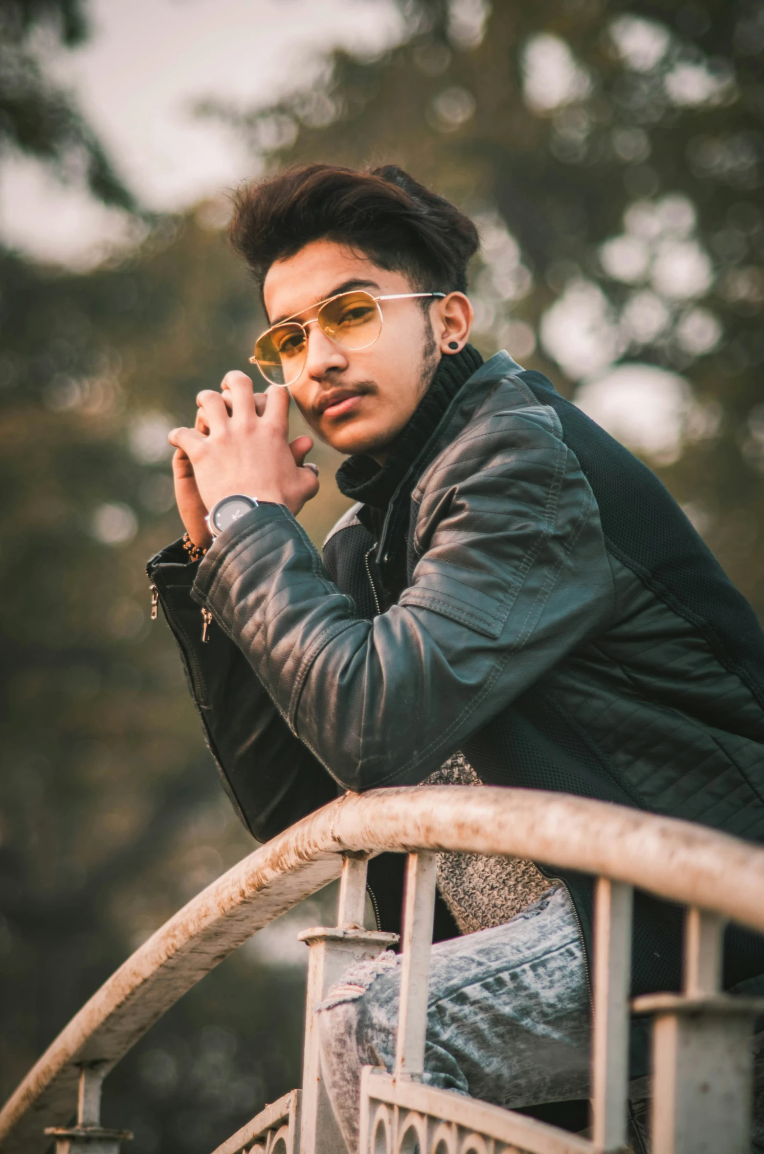 an indian man wearing sunglasses while sitting down on the railing