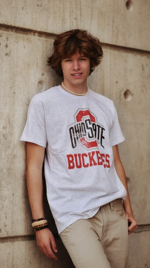 a young man leaning on a wall wearing a tee shirt