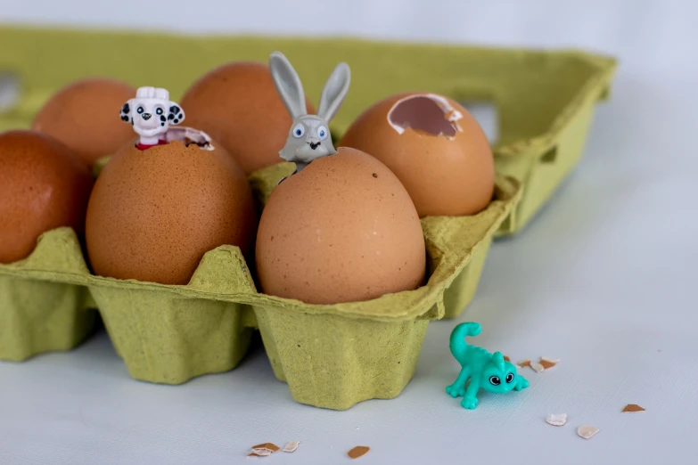 four easter eggs and three small figures in an egg carton