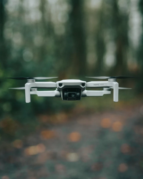 a white quadcopte flying over a forest