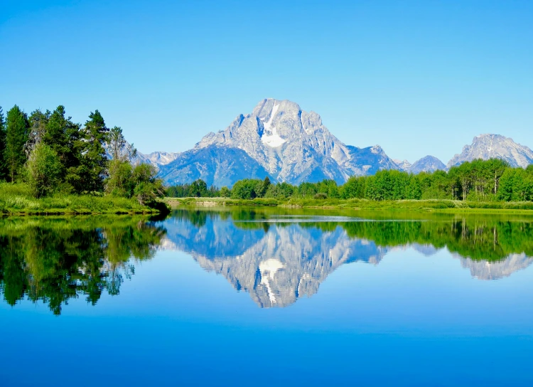 a mountain range with the reflection of some trees in water