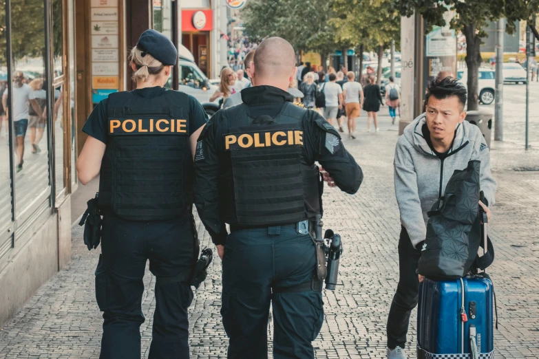 three policemen in a busy city street pulling luggage