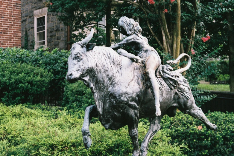 the statue of a woman on a cow in front of a house