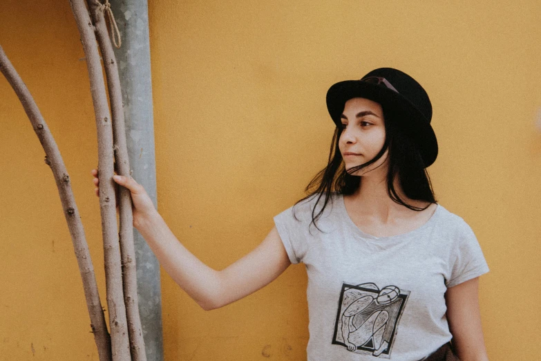 young woman wearing white shirt with black hat next to tree